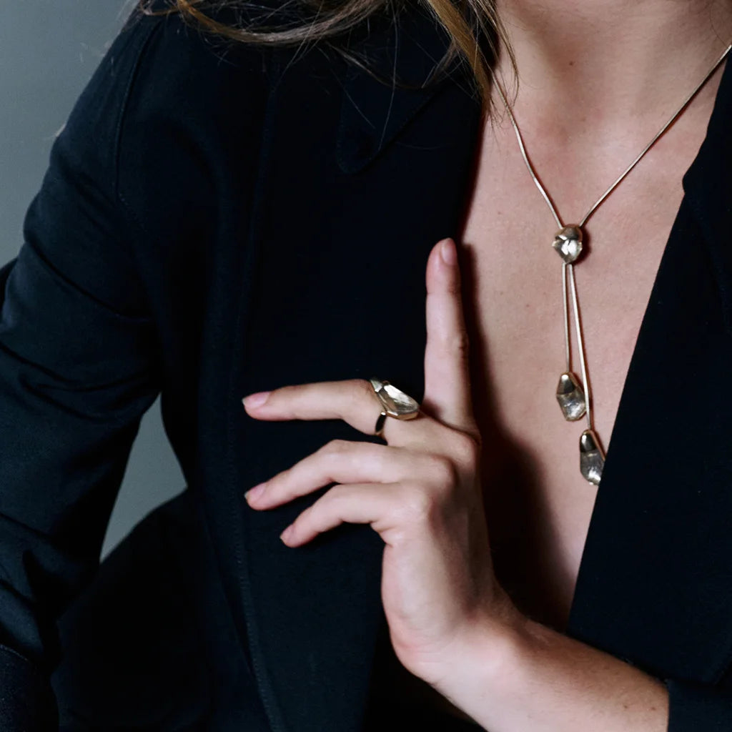 Une femme portant une bague cristal de roche Turbulence en métal doré assorti avec le collier cravate.