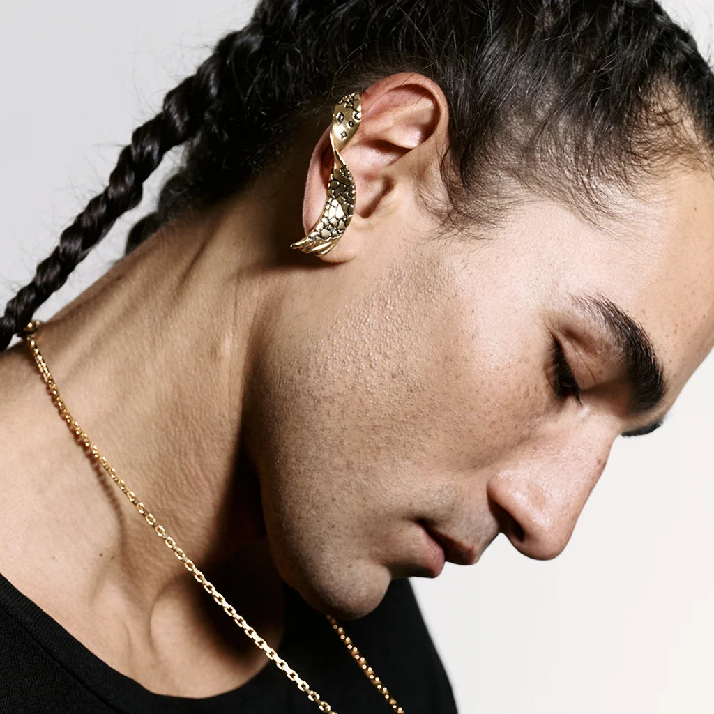 Un homme de profil portant un ear cuff Trouble en vieux doré à forme torsadée, accompagné d’un collier Trouble.