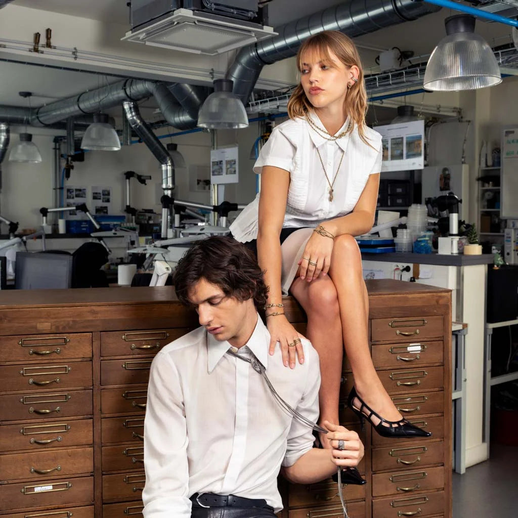 Photo portée de colliers, bracelet et bagues dorés portés en accumulation avec chemise blanche.