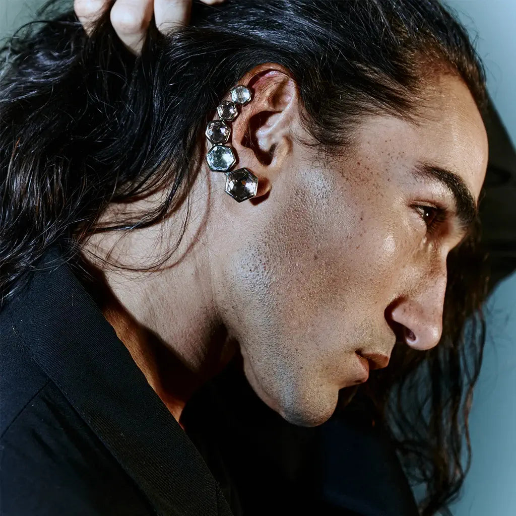 Un homme portant une boucle d'oreille strass Alma en métal satin argenté, rose et cristal.