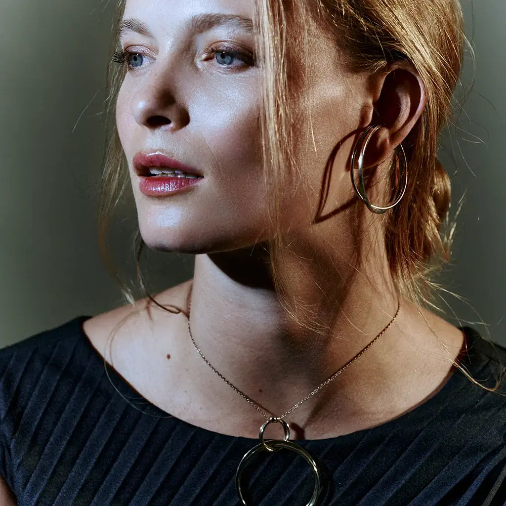 Une femme portant des anneaux oreilles femme Aurore en métal satin argenté assorti au collier