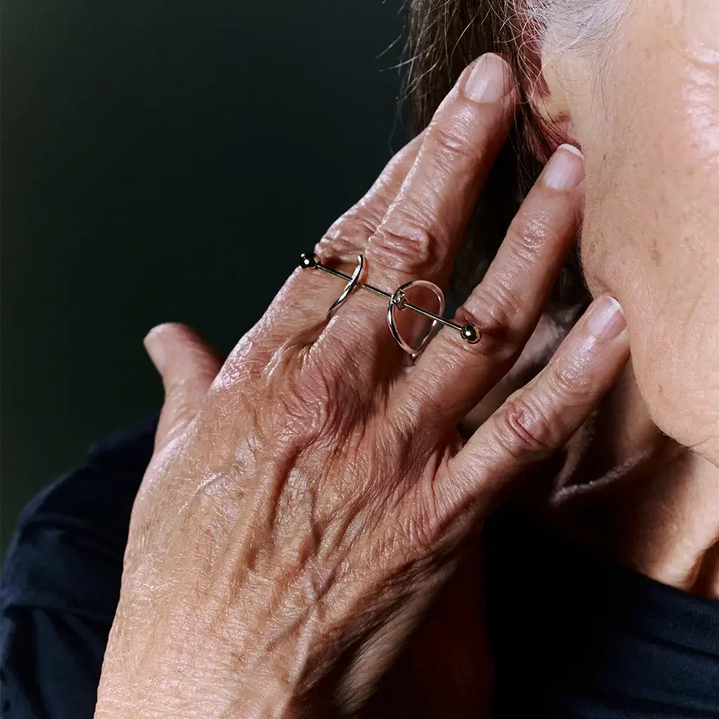Une femme portant une bague bicolore avec fibule Balem graphique, en métal satin argenté et doré brillant.