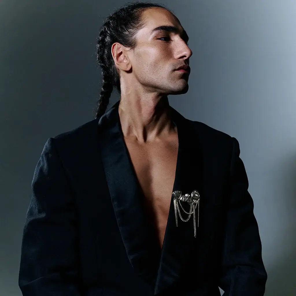 Un homme portant une grande broche Hortensia en métal satin ruthénium, ornée de strass et d’une cascade de chaînes.