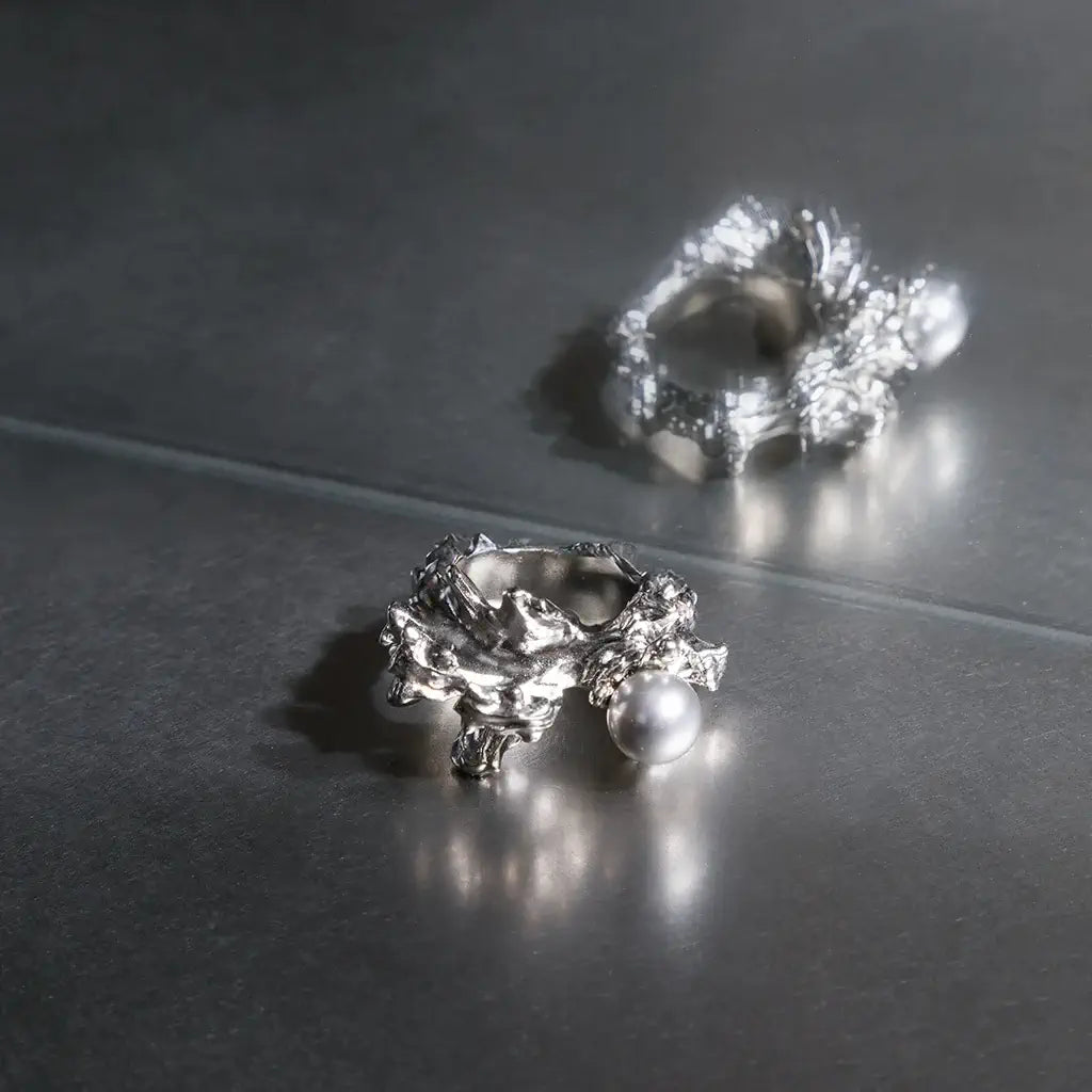 Une bague perle Nature en métal argenté texturé, ornée d’une perle grise en cristal laqué, de forme sculpturale, sur fond gris.