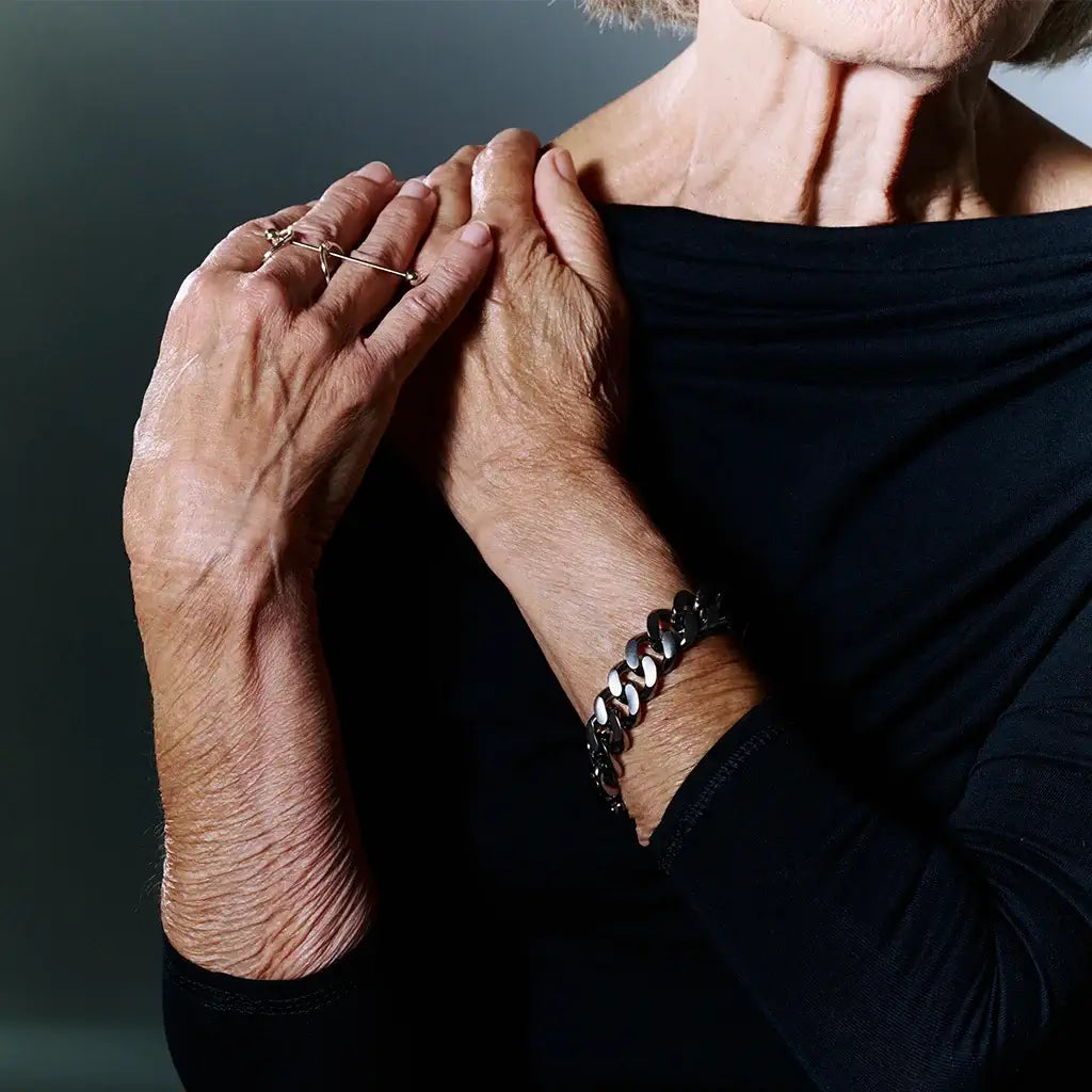 Une femme portant un bracelet chaîne homme Nebula en métal satin ruthénium, accompagné d’une bague.