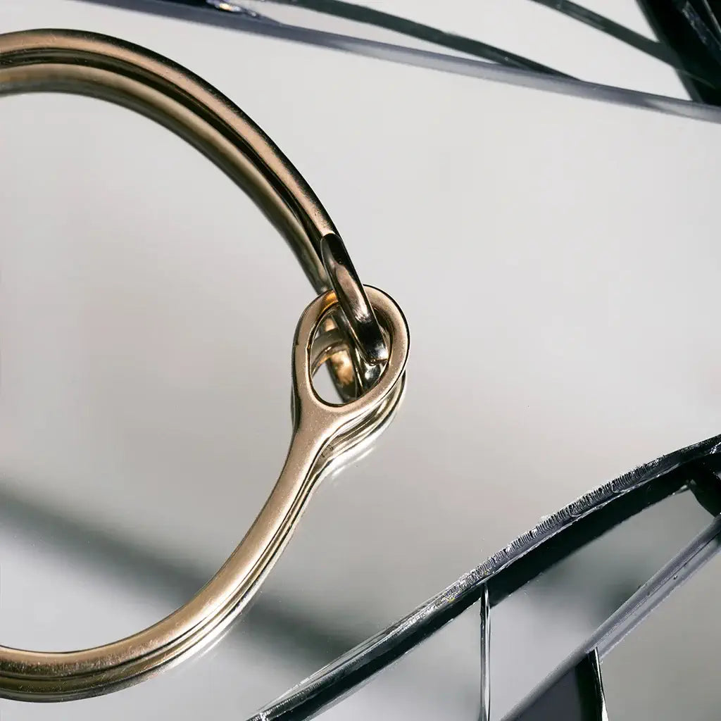 Un bracelet menotte Noe en zoom, en métal doré brillant, posé sur du verre en nature morte.