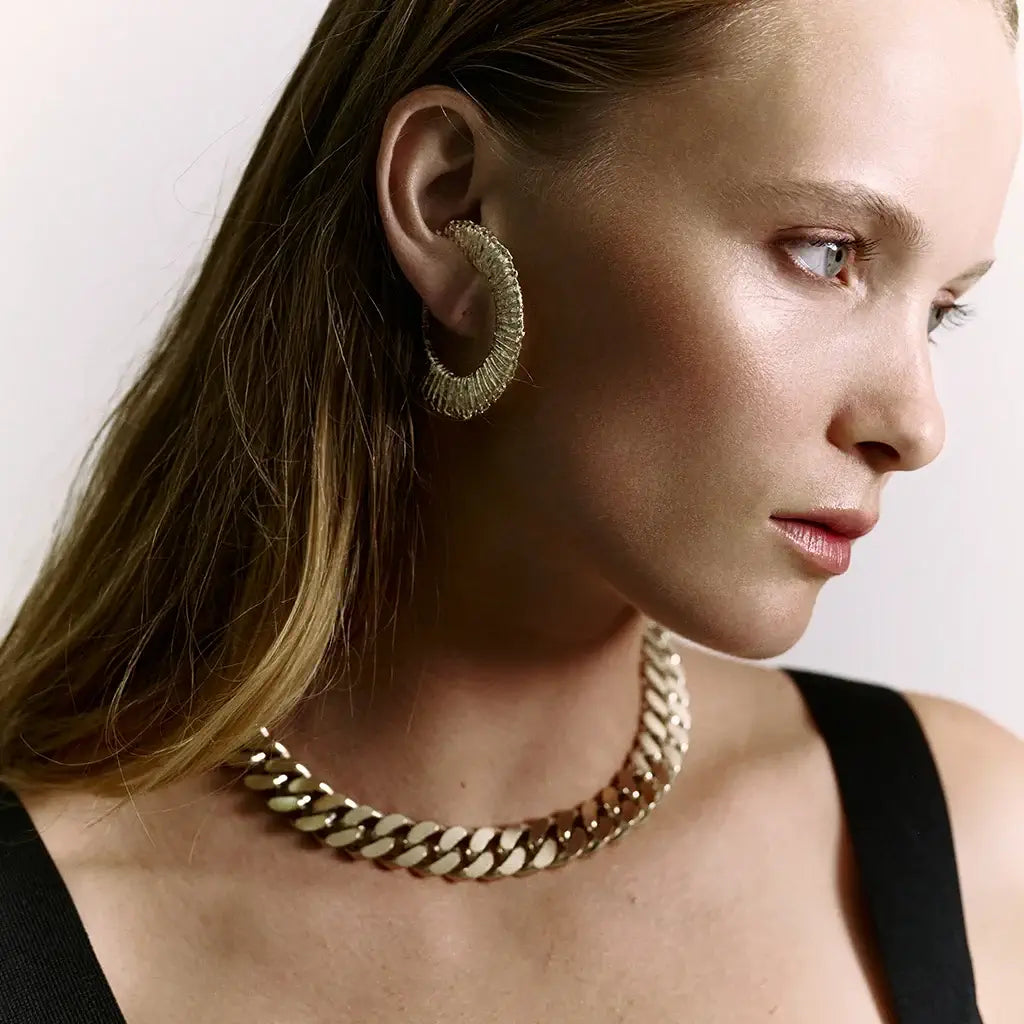 Une femme portant des boucles d’oreilles Spirale en métal satin doré, avec un collier chaîne Nebula assorti.