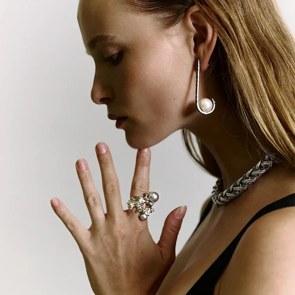 Une femme portant des boucles d’oreilles longues Valentina en métal vieilli, ornées d’une perle en cristal laqué.
