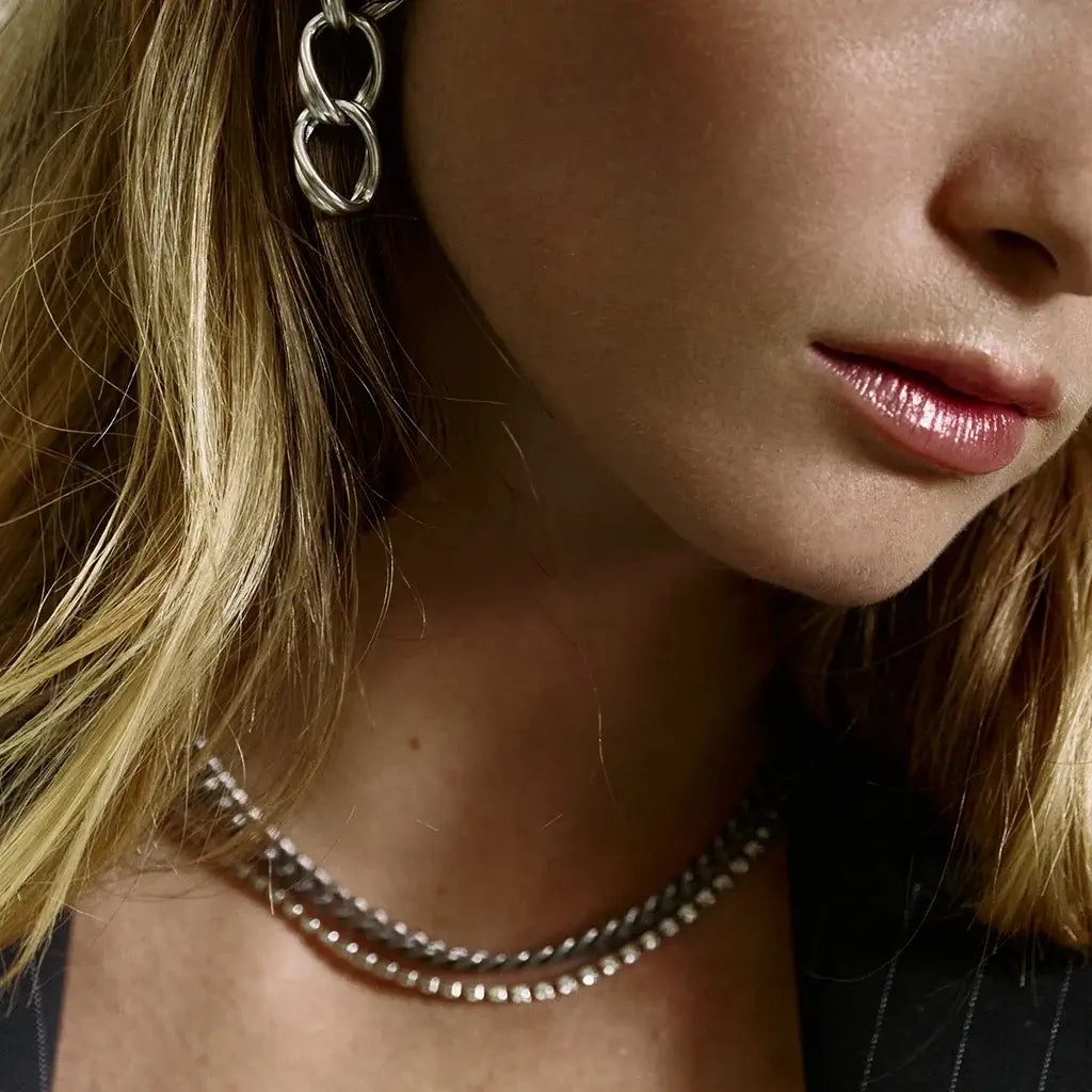 Femme portant le collier gourmette Vénus en métal argenté, combinant une chaîne texturée et une fine chaîne de strass.