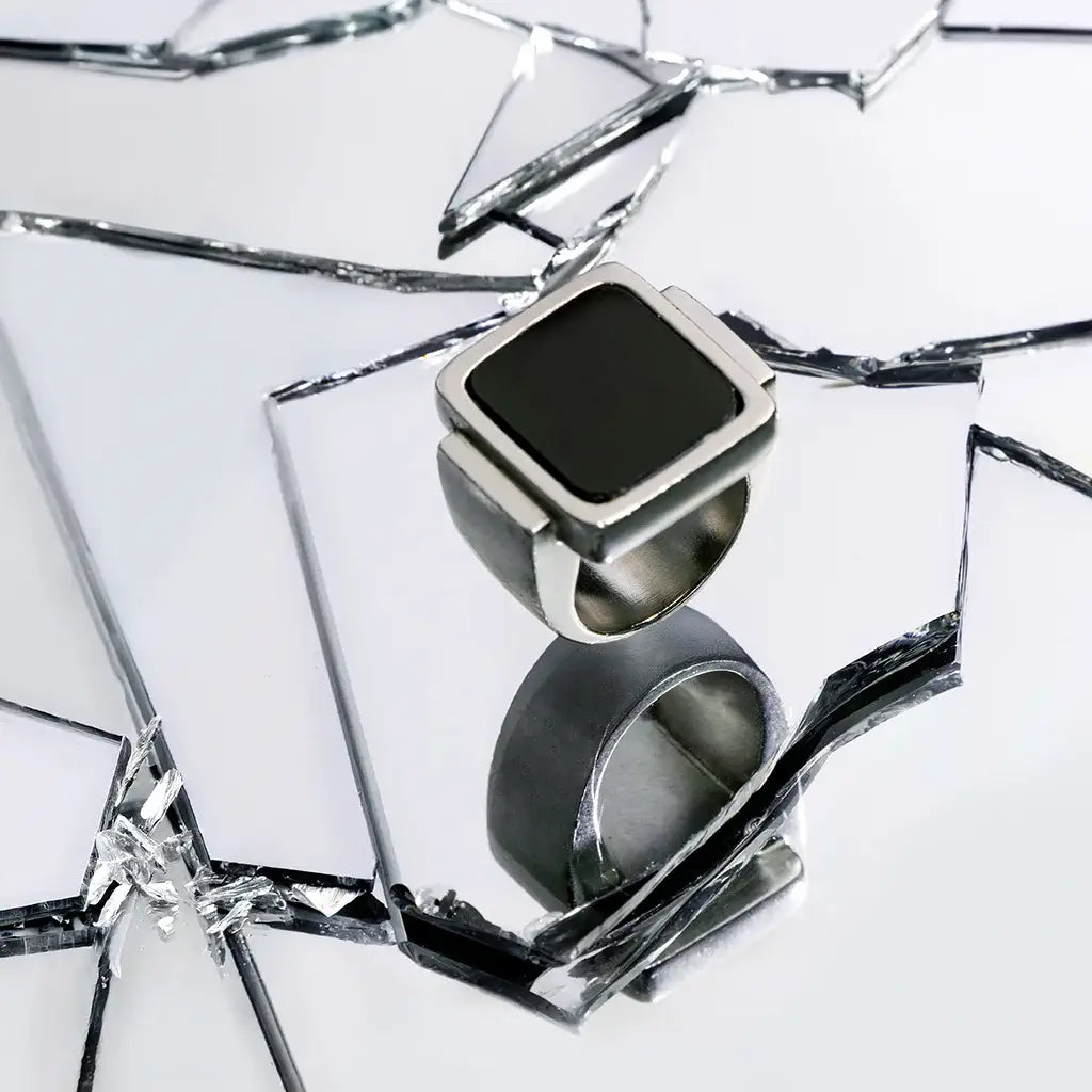 Une bague chevalière Wakanda en métal satin argenté et noir, posée en nature morte sur un fond aluminium.