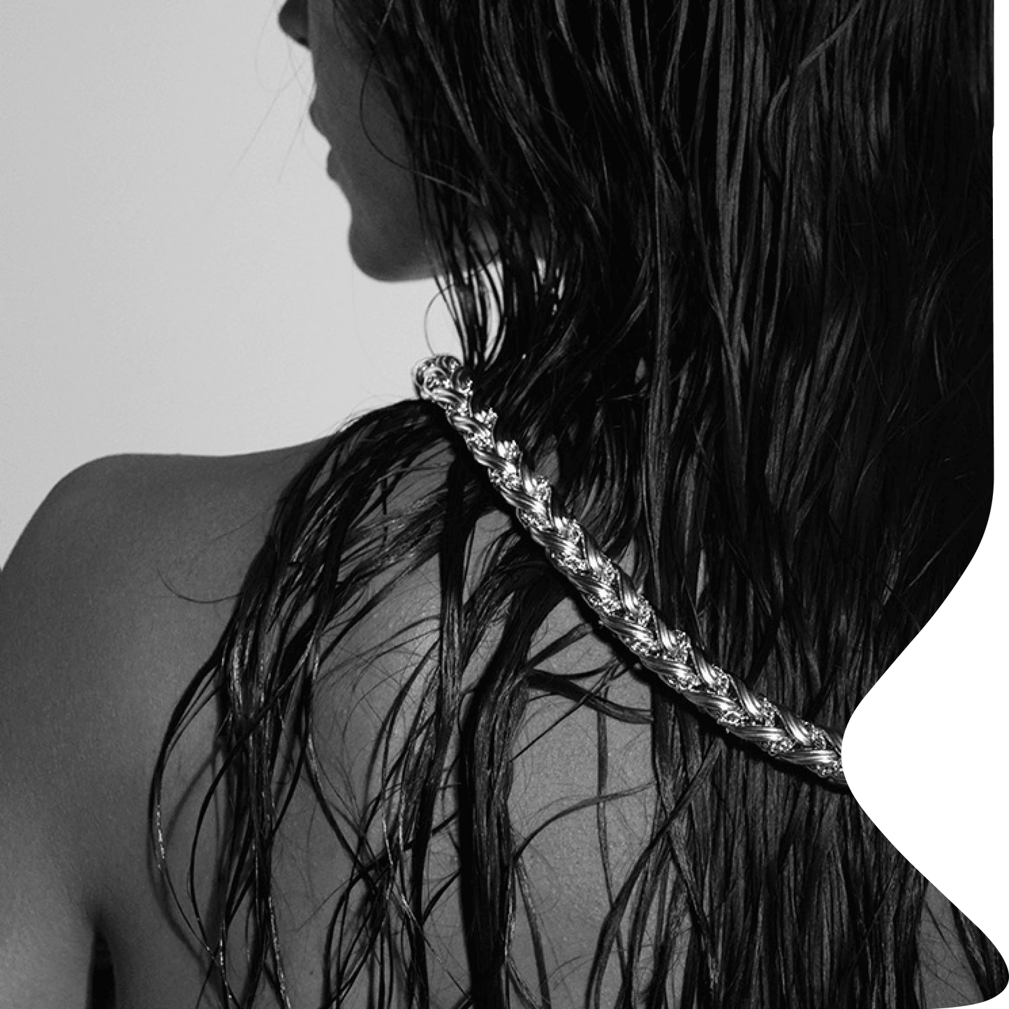 Femme de dos aux cheveux mouillés portant une chaîne torsadée argentée sur l’épaule dans une ambiance noir et blanc éditoriale.
