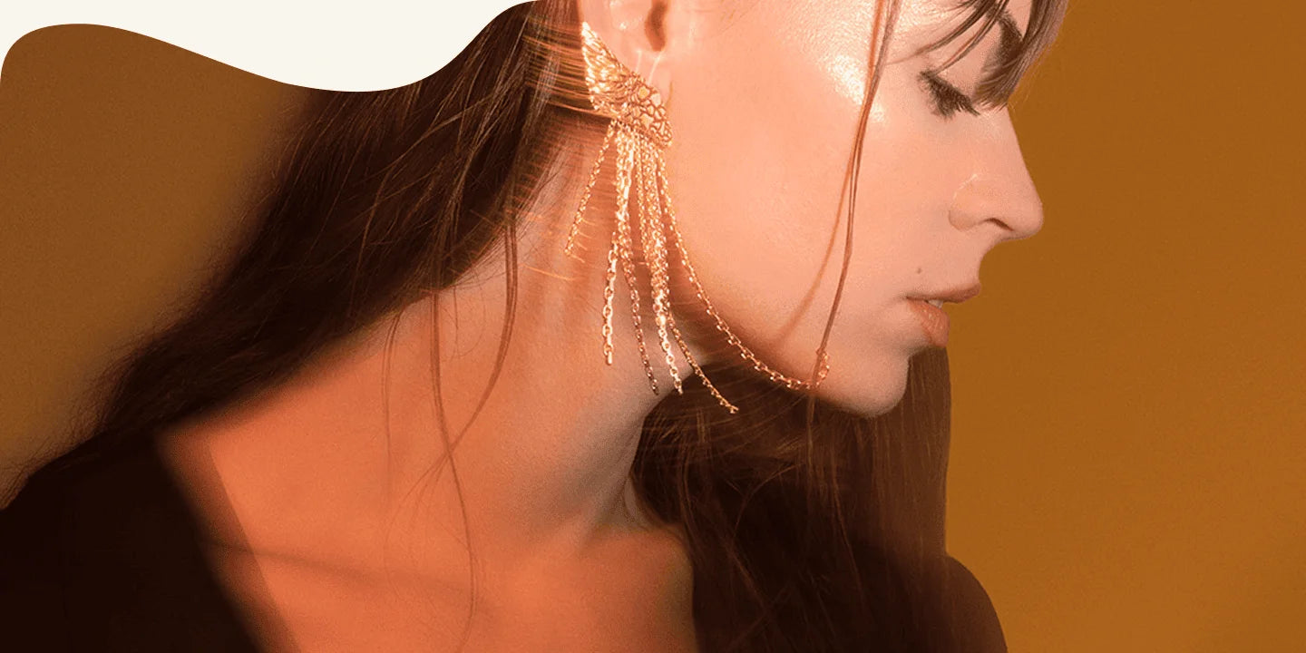 Photo portée de boucles d’oreilles dorées à chaînes pendantes avec effet de lumière et mouvement.